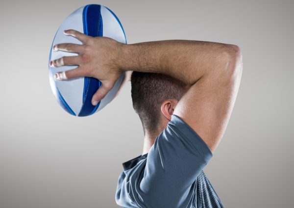 Man holding rugby ball against grey background